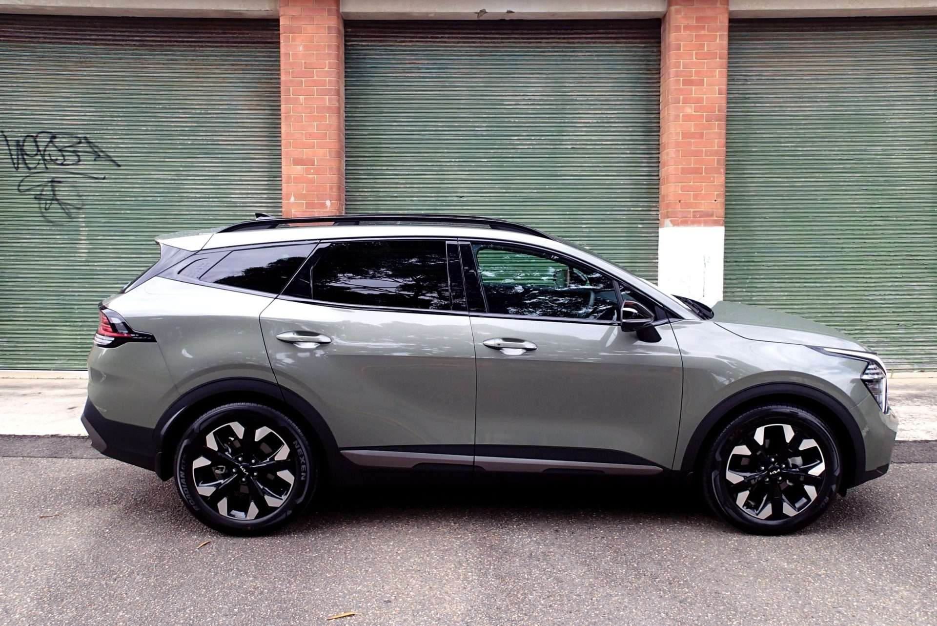 Kia Sportage GT-Line in Jungle Wood Green in front of a garage